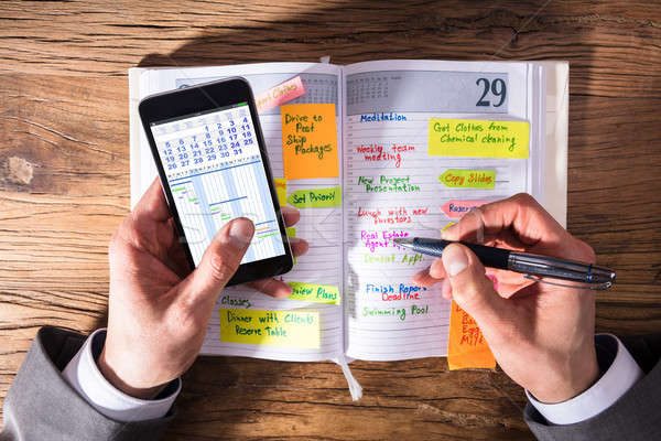 9086616_stock-photo-businessperson-with-mobile-phone-writing-schedule-in-diary